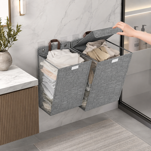 Corbeille à linge murale pliable en tissu gris à deux compartiments contenant des serviettes et des vêtements dans une salle de bain