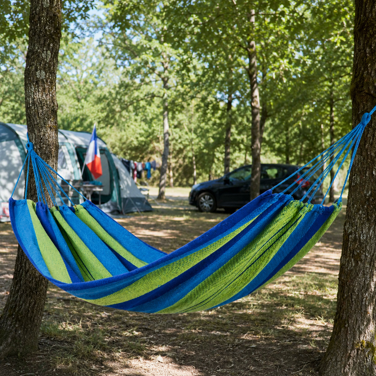 Hamac en toile rayée bleu et vert suspendu entre des arbres sur un terrain de camping