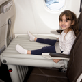 Lit de voyage gonflable pour enfants dans une cabine d’avion avec un enfant assis dessus portant des chaussettes blanches et un legging bleu marine